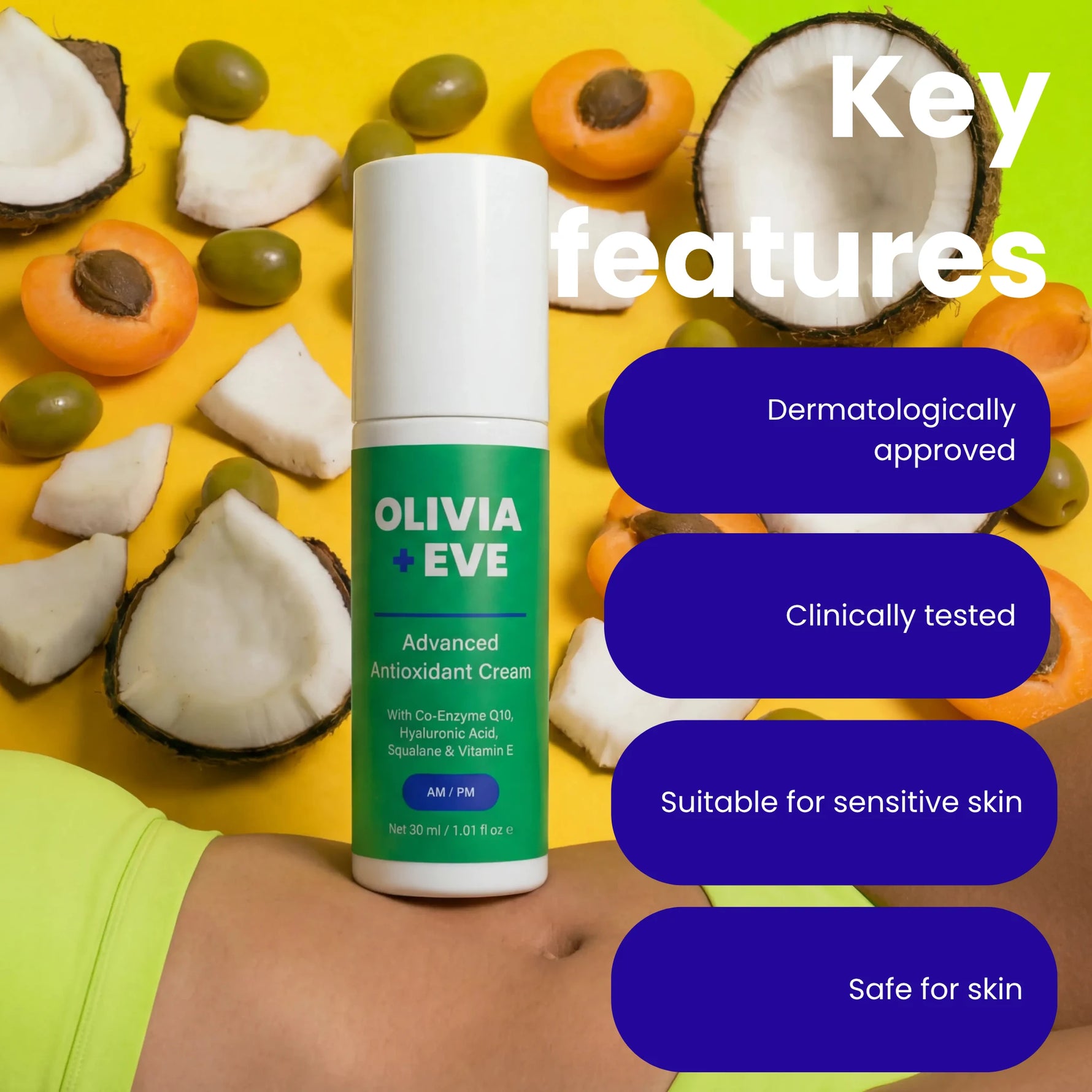 A bottle of Olivia + Eve Advanced Antioxidant Cream stands on a person's stomach against a bright yellow background with coconut halves, apricots, and olives scattered around. White text on the right reads 'Key features' with four dark blue callouts: dermatologically approved, clinically tested, suitable for sensitive skin, and safe for skin.