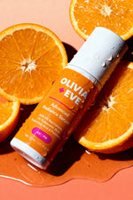 Olivia + Eve Advanced Radiance Serum bottle surrounded by sliced oranges on a peach background