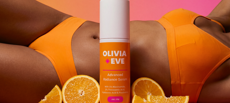 Woman in orange bikini with 'Olivia + Eve' product and oranges on a pink background
