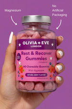 Hand holding a bottle of Olivia + Eve Rest & Recover Gummies against a purple background