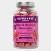 A clear plastic bottle of Olivia + Eve Rest & Recover Gummies with a purple and pink label, filled with pink chewable gummies, on a light gray background.