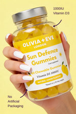 Hand holding a bottle of Olivia + Eve Sun Defence Gummies with lemon flavor on a yellow background