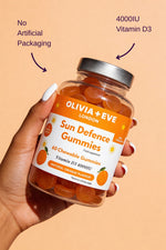 Hand holding a jar of Olivia + Eve Sun Defence Gummies with an orange background